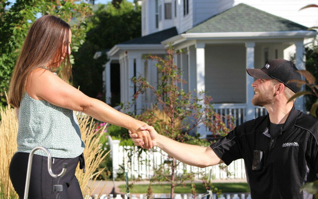 Home inspector shaking hands with a homeowner on a front porch, with neighboring houses blurred in the background.