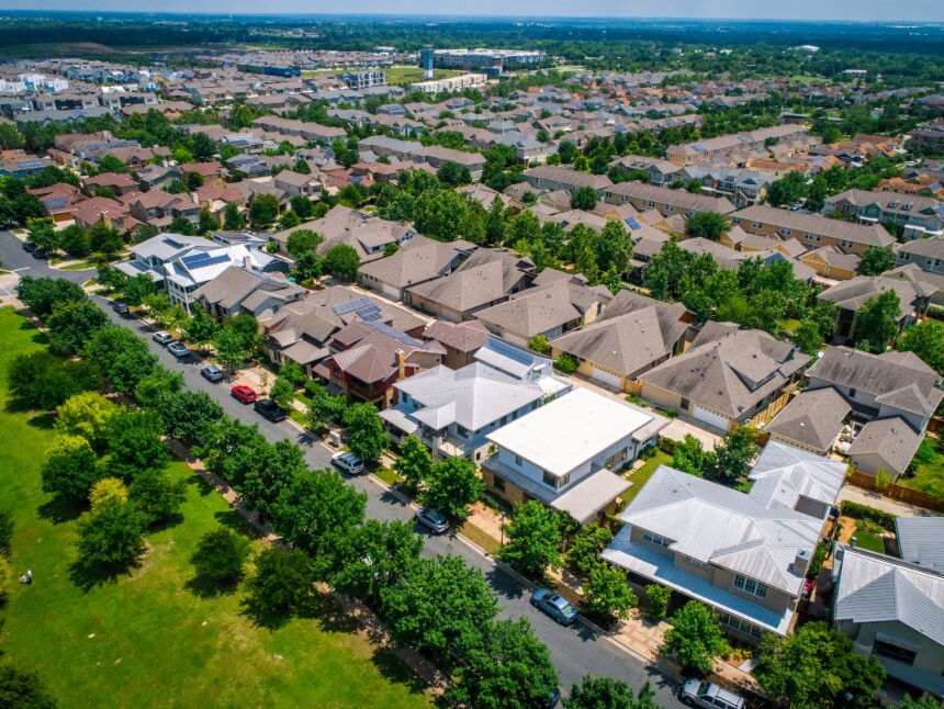 Aerial view of a dense suburban neighborhood showing a variety of residential rooftops, green lawns, and treelined streets.