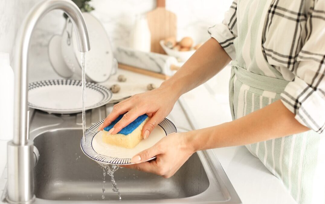 A person washing a plate under a running tap with a sponge.